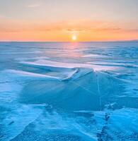 Winter landscape. A frozen surface of ice with snow intersected by many cracks. photo