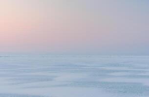 Winter landscape. A frozen surface of ice with snow intersected by many cracks. photo