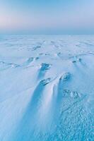Winter landscape. A frozen surface of ice with snow intersected by many cracks. photo