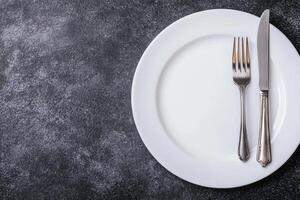 Empty white plate with silverware on dark background photo