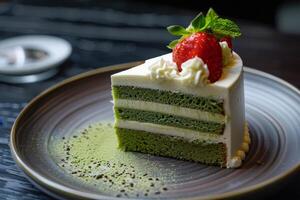 Delicious green tea cake garnished with a fresh strawberry and whipped cream on a dark plate photo