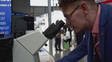 Man looks through microscope. Media. Man looks through new microscope at technology exhibition. New technologies with microscopes at Innovative Science Exhibition video