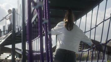 A joyful child plays on a colorful playground bridge under a sunny sky in an outdoor setting. Action video