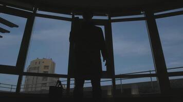 Dark silhouette of man with bag and phone. Stock. View from below of frightening silhouette of man with bag and phone. Dark shadow of man with bag pulls out phone on background of windows video