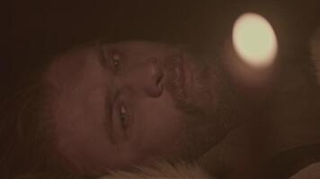 Close up of young bearded man closing eyes and falling asleep in a dark room with candlelight. Media. Pensive man lying and sleeping at night indoors. video