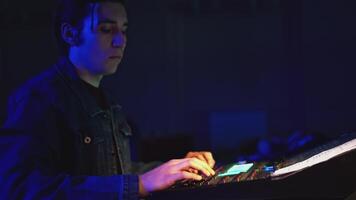 Man works at remote control of stage light and sound. Media. Young man controls light and sound behind stage. Stage technician at console video