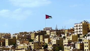Enjoy the stunning panoramic view of Amman with the iconic Jordanian flag on display. Action video