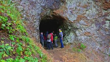Tourist group trip to cave. Clip. Group of tourists stands at entrance to cave and listens anxiously to briefing. Group hike with instructor to caves video
