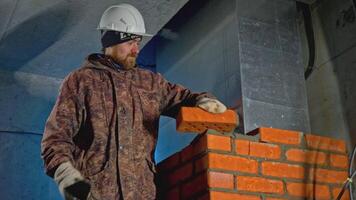 Man makes brickwork at construction site. Clip. Uniformed worker makes brickwork inside house. Man makes brick wall in house video