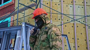 Man in work uniform speaks into walkie-talkie at construction site. Clip. Worker in helmet with walkie-talkie at construction site. Worker speaks into walkie-talkie at construction site video