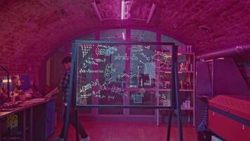 Young man solves equations in laboratory. Media. Student solves mathematical equations in secret classroom. Laboratory for experiments with mathematical calculations on blackboard video