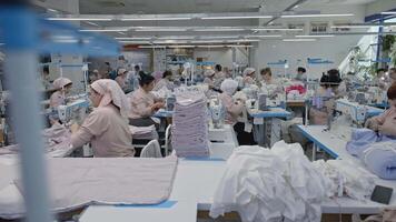 Manufacture of clothes in the large factory. Media. Factory employees are sewing clothes at the tables with machines. video