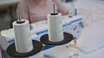Close up of white sewing threads are unwound from spools on a sewing machine. Media. Production sewing in a textile factory. video