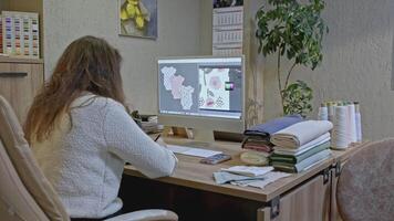 Female fashion designer in office making design of baby jumpsuit. Media. Using computer to create a pattern for children clothes. video