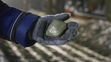 Worker holding piece of mined ore. Stock footage. Ore mining in industrial quarry with factory. Worker holds ore mined in production video