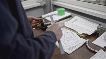 Worker measures part from drawings. Stock clip. Specialist makes measurements of metal part for project. Measurements and drawings of steel part at factory video