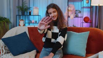 Child girl smiling friendly at camera, waving hands gesturing hello, hi, greeting at home on couch video