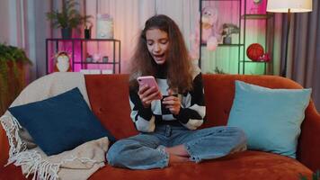 Lovely young girl at home use smartphone typing browsing, wow yes found out great big win celebrate video