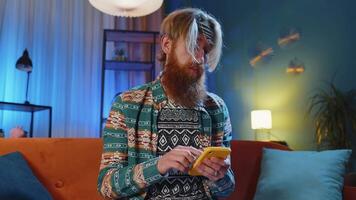 Portrait of adult man sitting on sofa, using smartphone share messages on social media application video