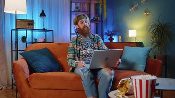 Man sitting on home couch, looking at camera, making conference call with friends or family video