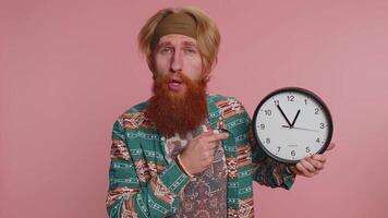 Bearded young man showing time on clock watch, ok, thumb up, approve, pointing finger at camera video