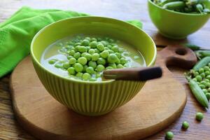 Fresh green pea soup with pea seeds and pea pods around . Selective Focus, Focus on the pea in the middle of the soup photo