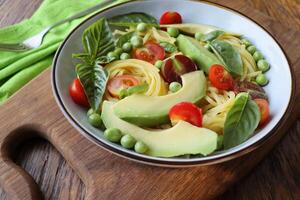 Pasta salad with green peas, avocado, cherry tomatoes and basil on rustic wooden background. Top view photo