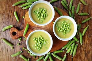 Fresh green pea soup with pea seeds and pea pods around . Selective Focus, Focus on the pea in the middle of the soup. Top view photo