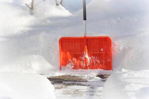 Snow cleaning concept. Red, orange shovel and snow during snowstorm. City ervice cleaning snow winter with shovel after snowstorm yard photo