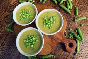 Fresh green pea soup with pea seeds and pea pods around . Selective Focus, Focus on the pea in the middle of the soup photo