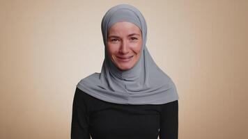 Muslim woman in hijab smiling friendly at camera, nods her head gesturing hello hi, assalamu alaikum video