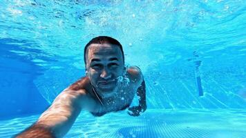 Swimming underwater man in pool. Man doing underwater selfie shot in pool video