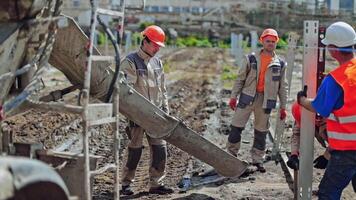 Workers at construction site. Worker leveling concrete poured from mixer on construction site video