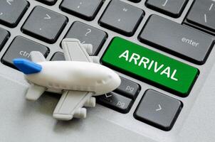 Top view of Arrival text on laptop keyboard with airplane toy background. Travel and destination concept photo