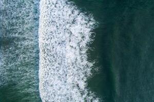 view of a wave on the shore of a beach at sunrise, and people surfing. Aerial top view photography with a drone. photo