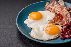 English breakfast with fried eggs, bacon, beans, tomatoes, spices and herbs photo