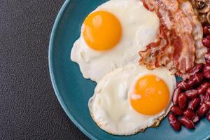 English breakfast with fried eggs, bacon, beans, tomatoes, spices and herbs photo