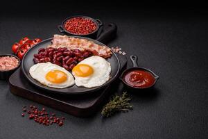 English breakfast with fried eggs, bacon, beans, tomatoes, spices and herbs photo