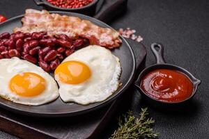 English breakfast with fried eggs, bacon, beans, tomatoes, spices and herbs photo