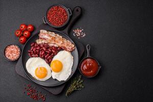 English breakfast with fried eggs, bacon, beans, tomatoes, spices and herbs photo