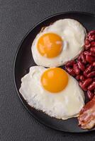 English breakfast with fried eggs, bacon, beans, tomatoes, spices and herbs photo