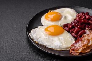 English breakfast with fried eggs, bacon, beans, tomatoes, spices and herbs photo