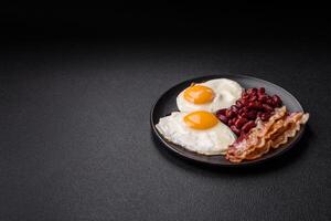 English breakfast with fried eggs, bacon, beans, tomatoes, spices and herbs photo