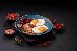 English breakfast with fried eggs, bacon, beans, tomatoes, spices and herbs photo