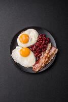 English breakfast with fried eggs, bacon, beans, tomatoes, spices and herbs photo