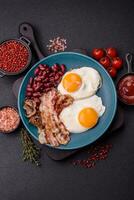 English breakfast with fried eggs, bacon, beans, tomatoes, spices and herbs photo