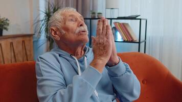 Senior man praying sincerely with folded arms asking God for help, begging apology, making a wish video