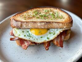 Breakfast sandwich with egg and bacon served on toasted bread photo