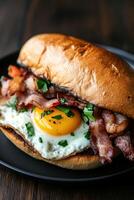 Delicious breakfast sandwich with bacon, egg, and herbs served on a bun photo
