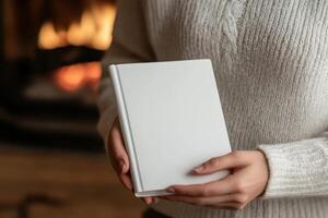Person holding a blank notebook near a cozy fireplace photo